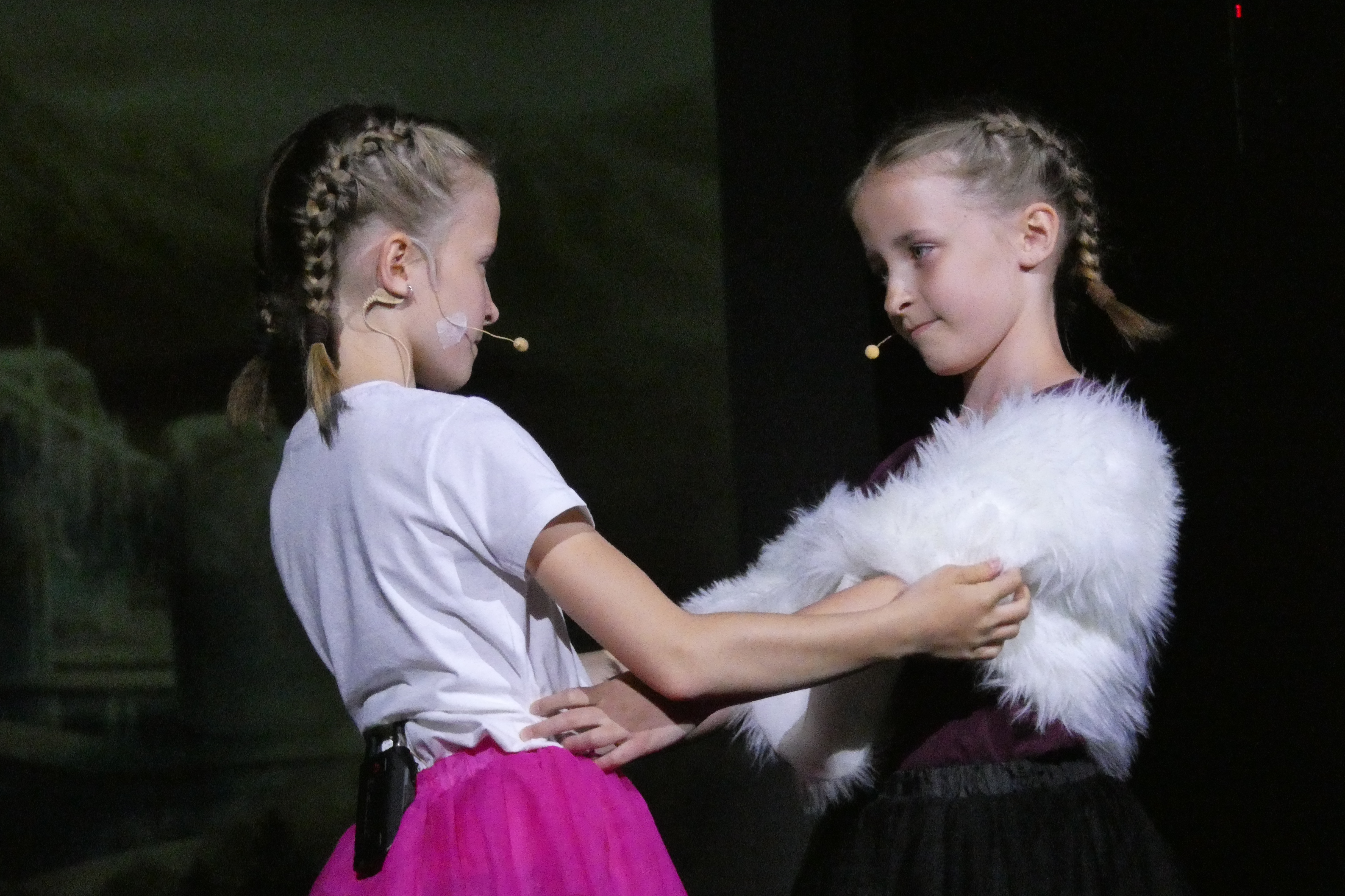 Na zdjęciu widoczne są dwie uczennice stojące przodem do siebie, mające wyciągnięte do siebie ręce.