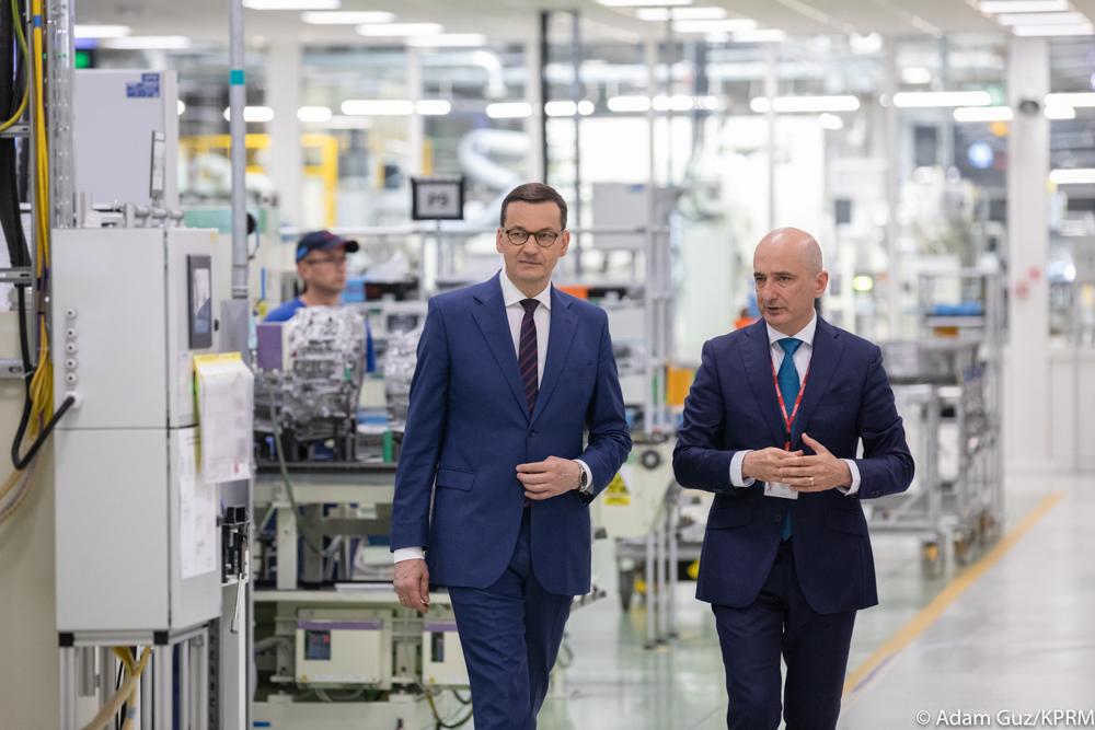 Premier Mateusz Morawiecki idzie, a w tle pomieszczenie fabryki.