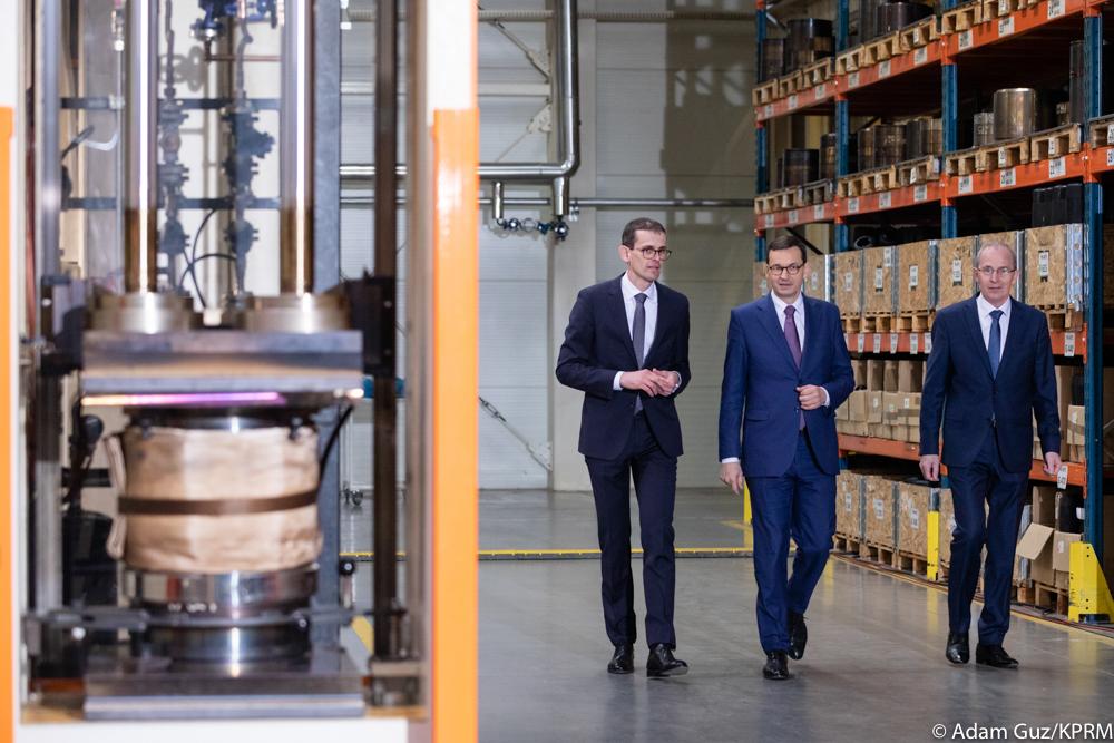 Premier Mateusz Morawiecki i prezesi firmy idą między regałami.