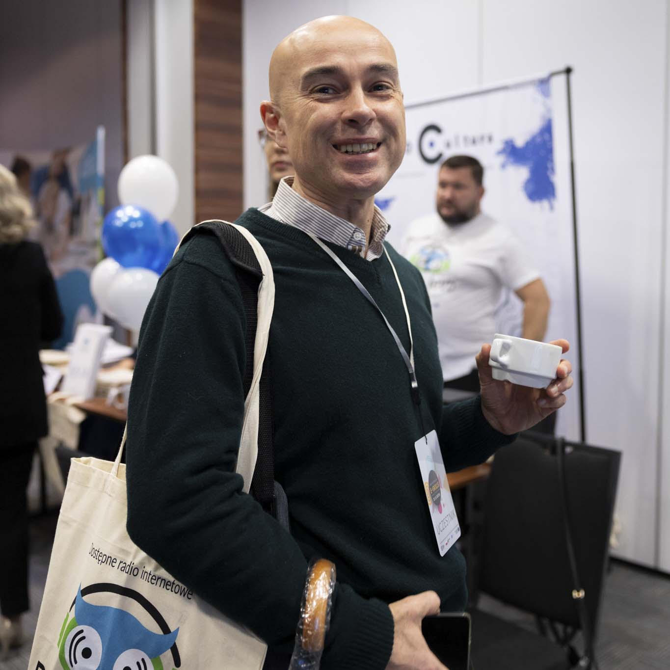 Uśmiechnięty uczestnik konferencji stoi, patrzy w obiektyw.