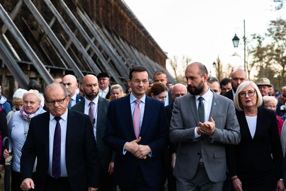Premier Mateusz Morawiecki przechadza się przy termach w Ciechocinku, za nim tłum ludzi.