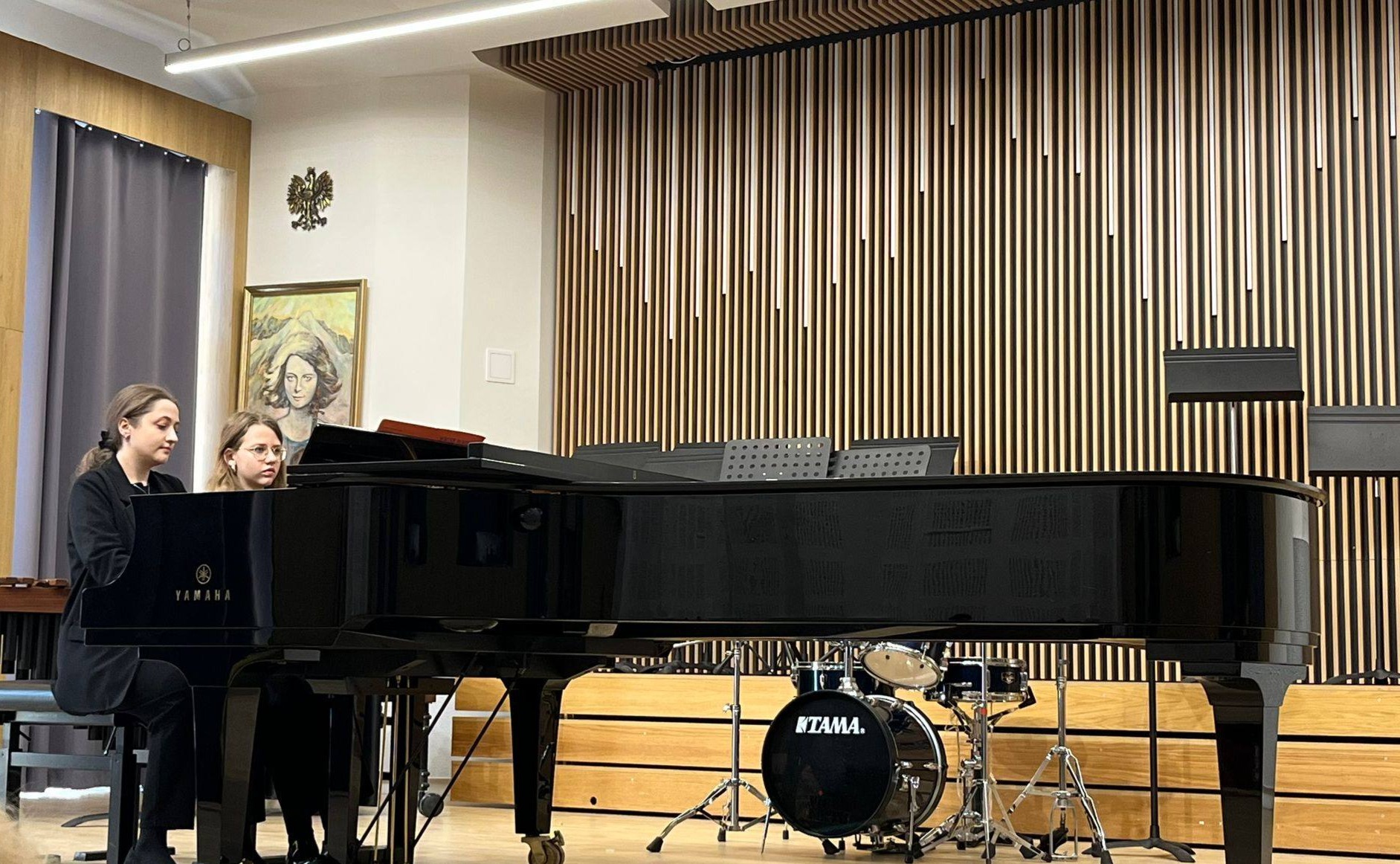 Na scenie fortepian oraz dwie pianistki grające utwór.