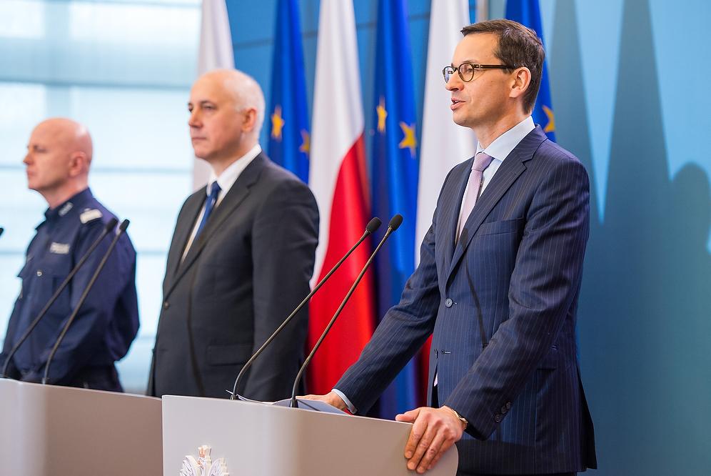 Premier Mateusz Morawiecki przy mównicy, w tle minister Joachim Brudziński oraz Komendant Główny Policji.