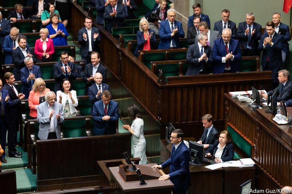 Premier przy mównicy, posłowie biją brawo.