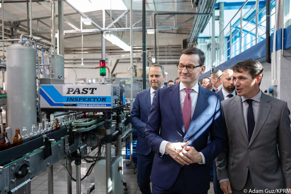 Premier Mateusz Morawiecki patrzy na butelki wody na taśmie produkcyjnej.