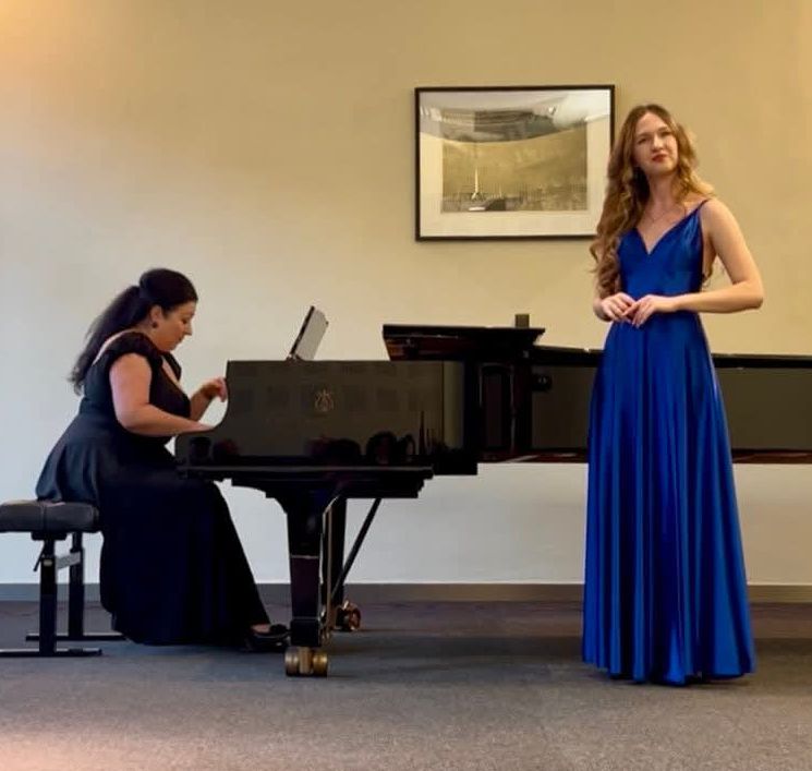 Amelia Szmidt na scenie konkursu w dn. 17.04.2026. Uczennica w niebieskiej sukni, w tle akompaniatorka.