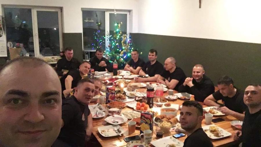 Zdjęcie grupowe strażaków z jednostki ratowniczo gaśniczej numer 1 w Elblągu podczas wigilijnej kolacji. Strażacy zasiadają przy stole na którym stoją wigilijne potrawy.