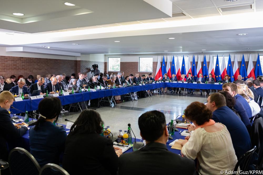 Okrągły stół i siedzący przy nim ludzie.