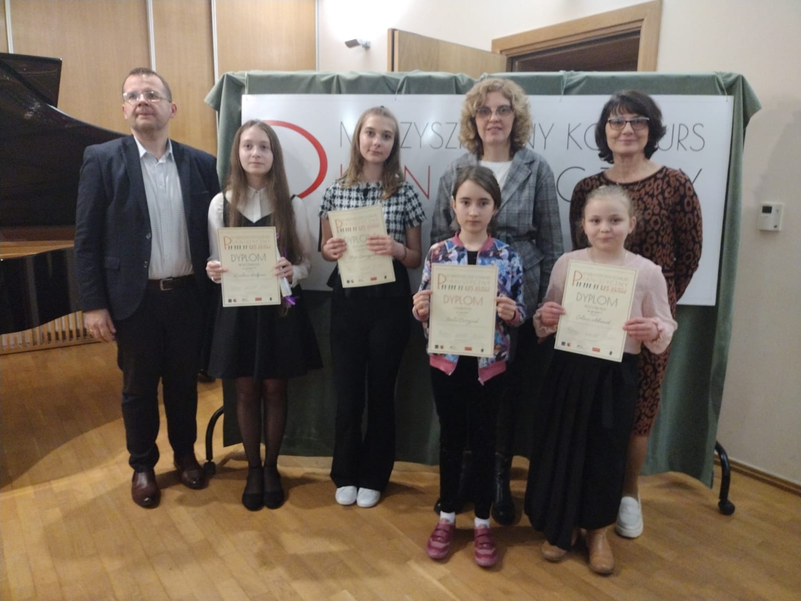 Zdjęcie przedstawia uczennice klasy fortepianu naszej szkoły wraz ze swoimi nauczycielami. Uczennice trzymają w rękach zdobyte dyplomy.