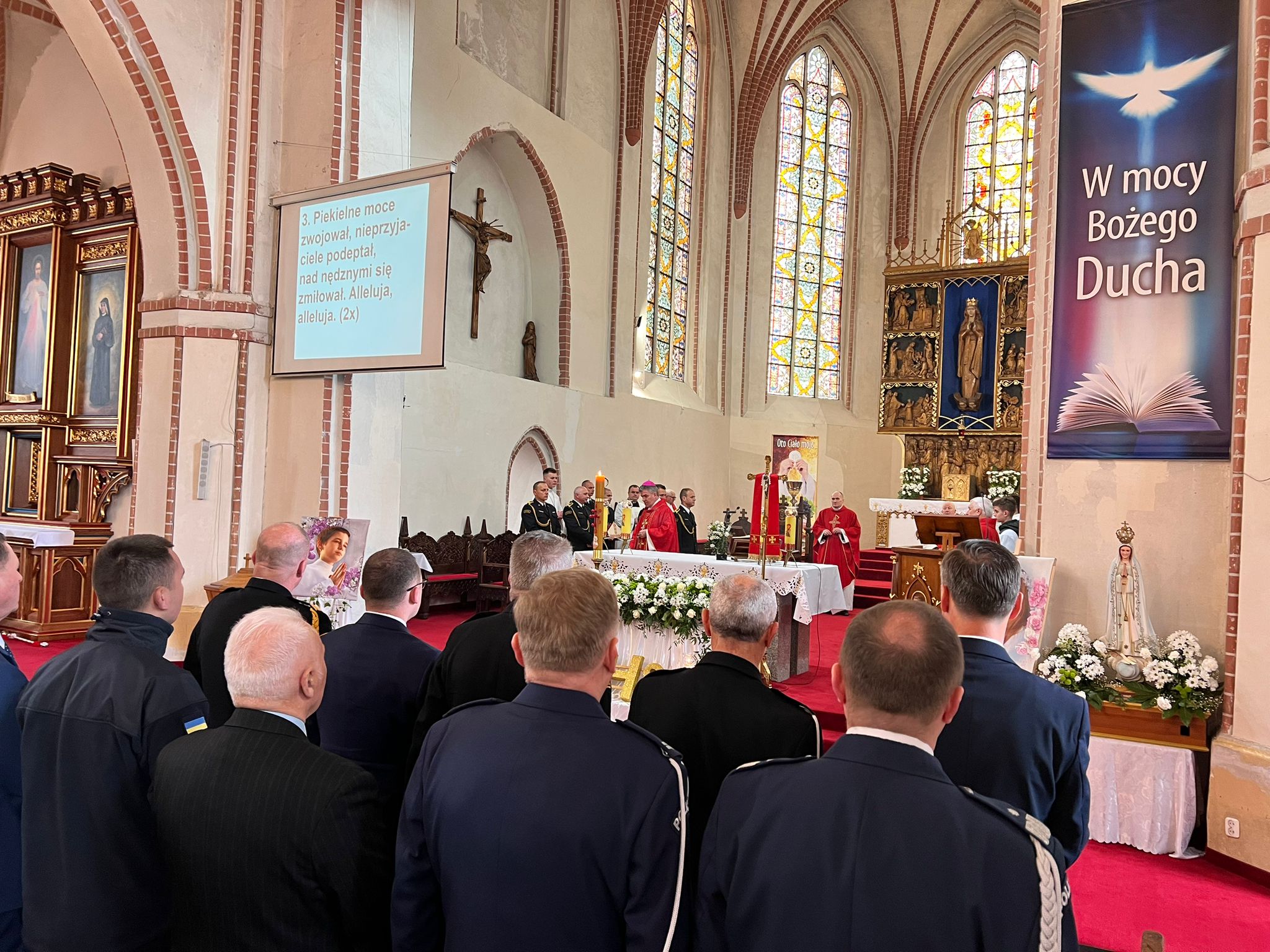 W kościele stoją uczestnicy mszy Świętej, strażacy i osoby cywilne(widok z tyłu), przed nimi ołtarz i księża