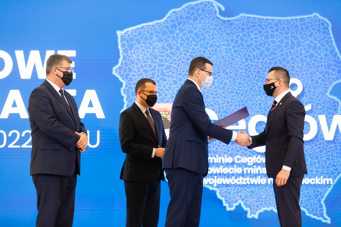 Na zdjęciu widać wiceministra Pawła Szefernakera, wiceministra Macieja Wąsika i premiera Mateusza Morawieckiego składającego gratulacje jednemu z przedstawicieli gmin która otrzymała akt nadania statusu miasta.