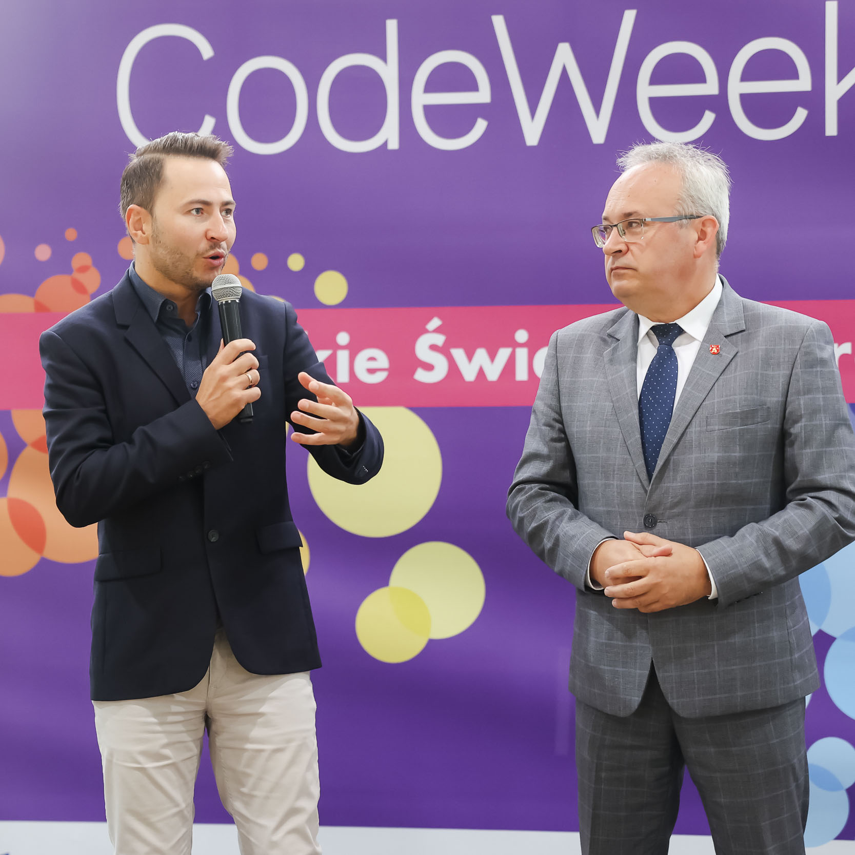 Przemawiający na tle ścianki Codeweek moderator wydarzenia, obok niego Burmistrz Augustowa Mirosław Karolczuk