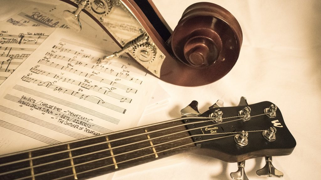 Zdjęcie. Na stylowanym na retro tle widać rozłożone nuty na nich leżą instrumenty. Widoczne tylko gryfy: gitary oraz ślimak i kołki kontarbasu