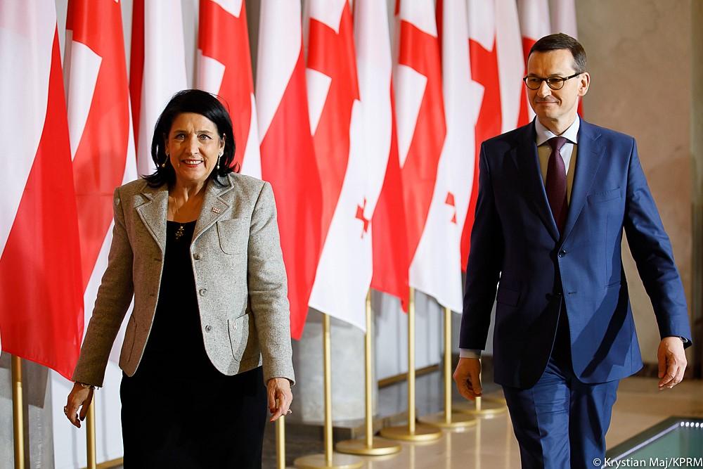 Prezydent Gruzji i premier Morawiecki idą na tle flag.