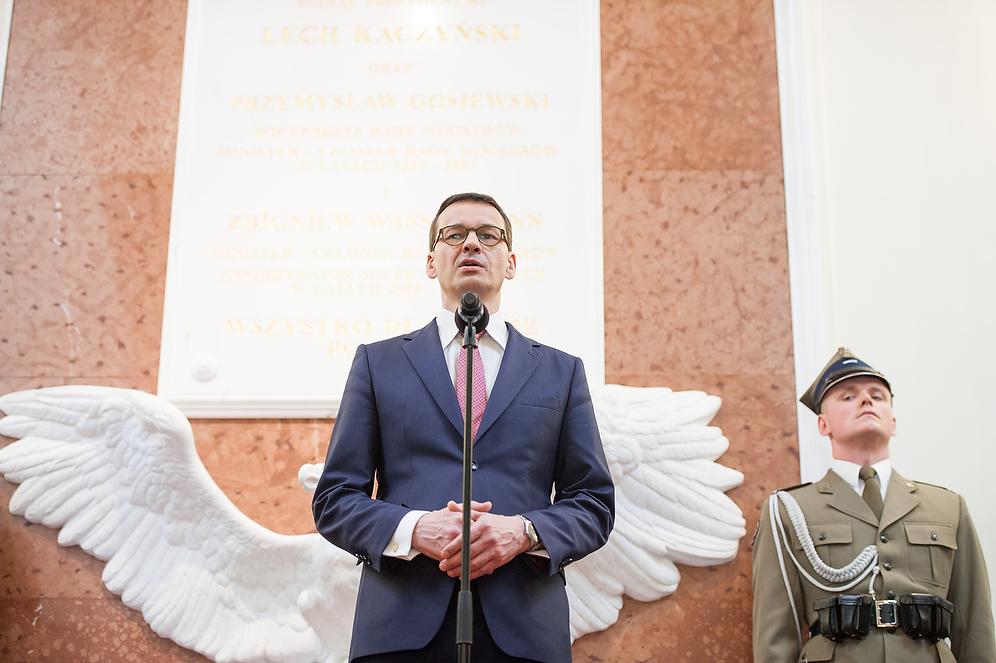 Premier Mateusz Morawiecki podczas przemówienia, a w tle tablice.