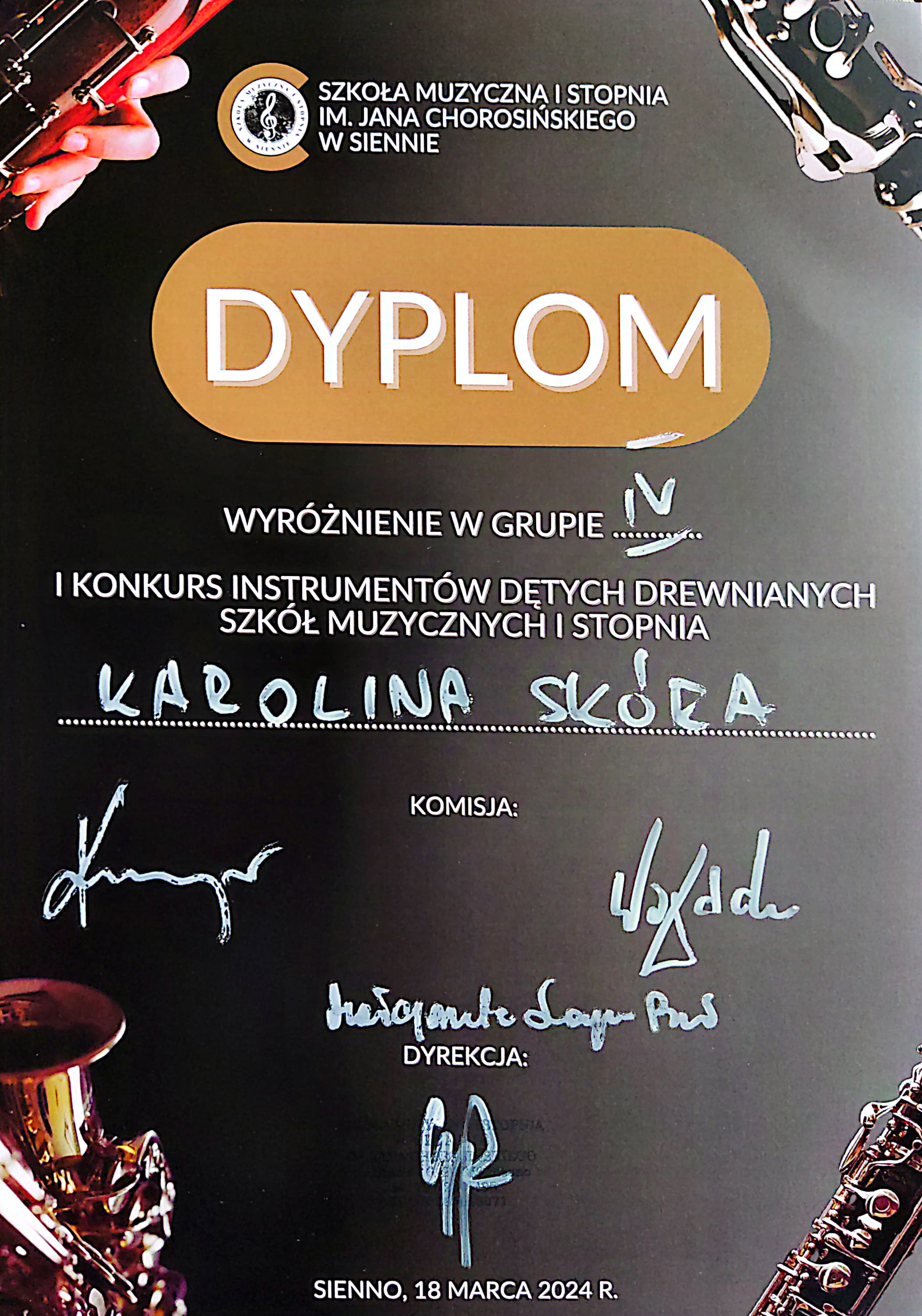 Na czarnym tle w rogach umieszczone fragmenty zdjęć instrumentów dętych drewnianych" fagot, klarnet, saksofon i obój. Na środku u góry logo szkoły i napis Szkoła Muzyczna I stopnia in. Jana Chorosińskiego w Siennie. Poniżej na jasnobrązowym tle napis Dyplom. Pod spodem biały napis wyróżnienie w grupie IV. I konkurs instrumentów dętych drewnianych szkół muzycznych I stopnia Ignacy Flis. Poniżej napis komisja i podpisy komisji, poniżej napis dyrekcja i podpis. Na dole napis Sienno, 18 marca 2024 r.