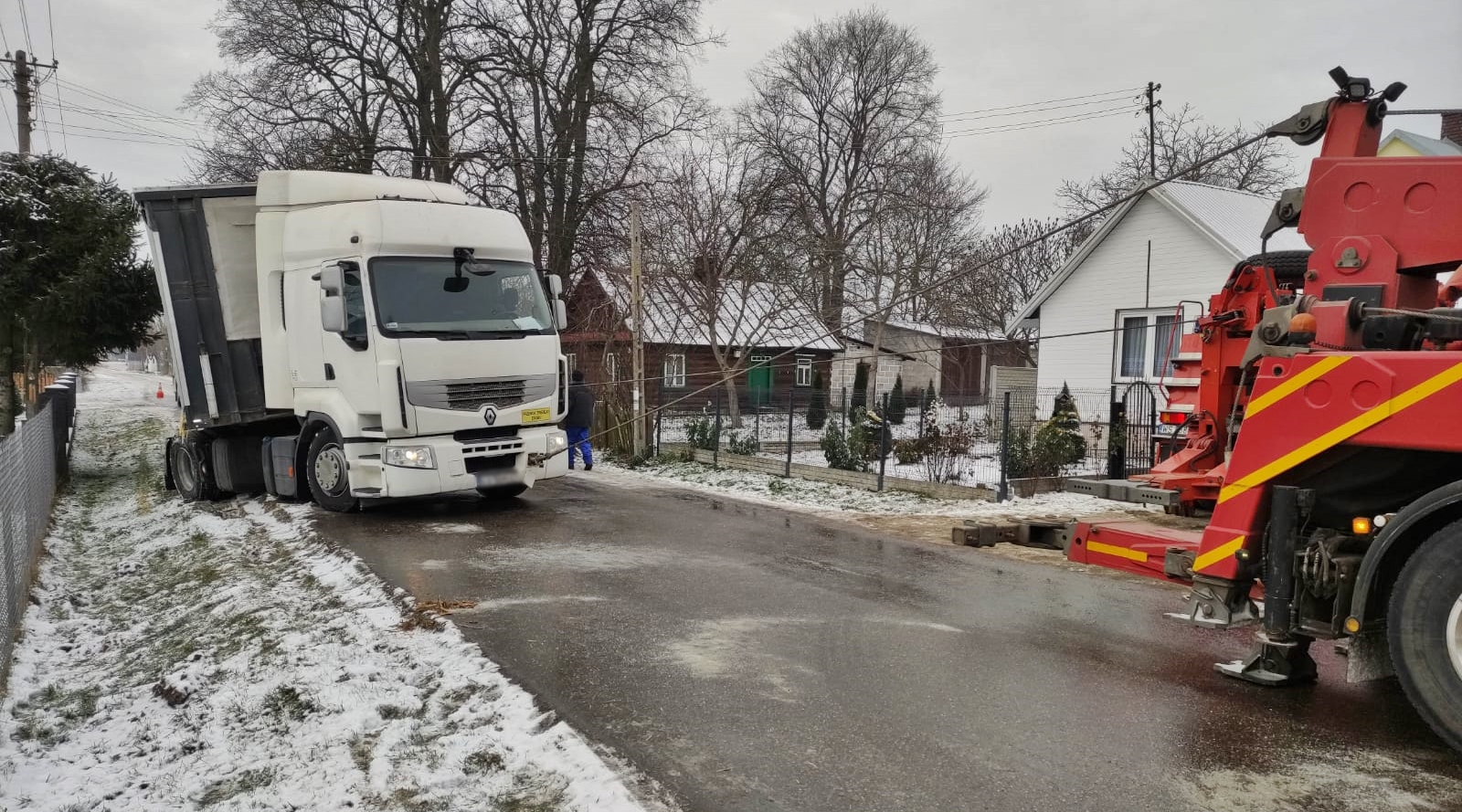 Na zdjęciu samochód ciężarowy, który zsunął się z drogi na pobocze. Strażacy z pomocą wyciągarek samochodowych wyciągają pojazd na drogę.