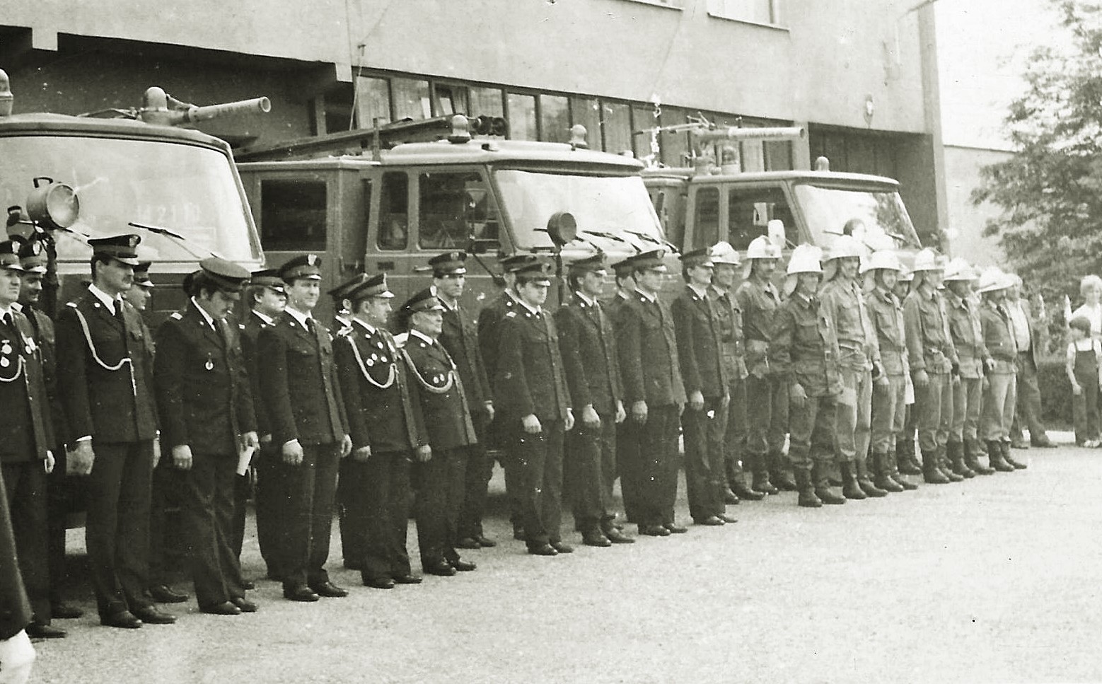 Na historycznym zdjęciu zbiórka strażaków z okazji obchodów Dnia Strażaka. W tle samochody oraz budynek KP PSP