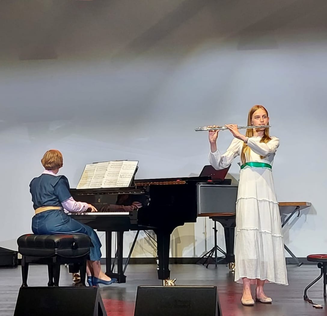 Zdjęcie z Koncertu MUZOMAN - 8.12 2017 na sali koncertowej PSM w Lubaczowie. Na zdjęciu siedzący chór i grająca sekcja dęta wraz z fortepianem.