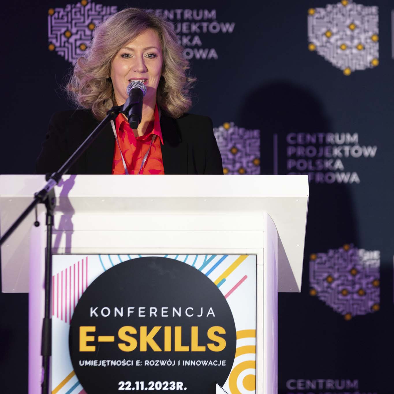 Przy mównicy stoi Pani Edyta Kraska. Wzrok kieruje w kierunku uczetników konferencji. Mówi do mikrofonu.