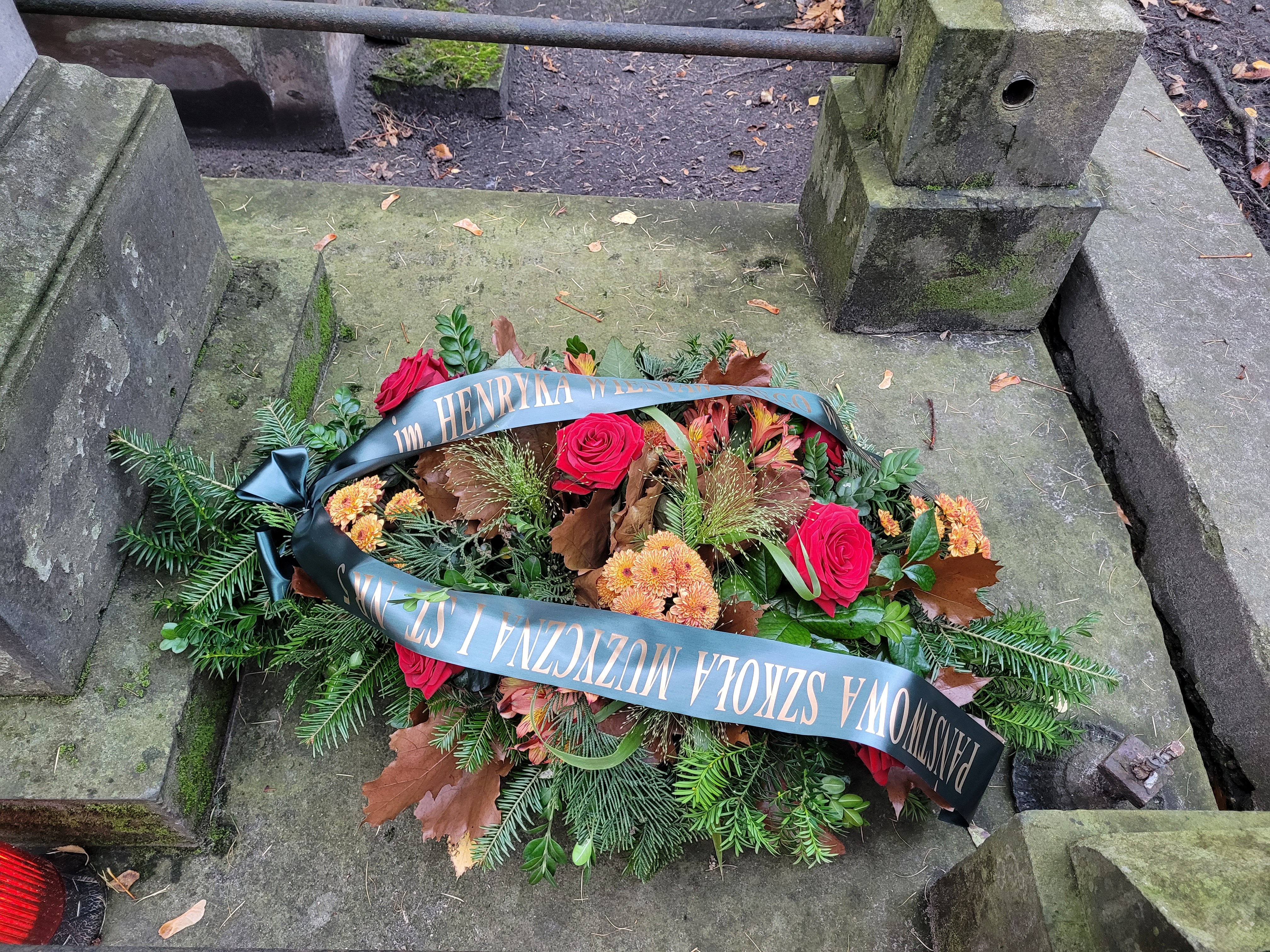 Zdjęcie wiązanki kwiatów, złożonej na grobie Henryka Wieniawskiego na cmentarzu Powązkowskim w Warszawie. Na wiązance szarfa z napisem: "Państwowa Szkoła Muzyczna I st. nr 5 im. Henryka Wieniawskiego".