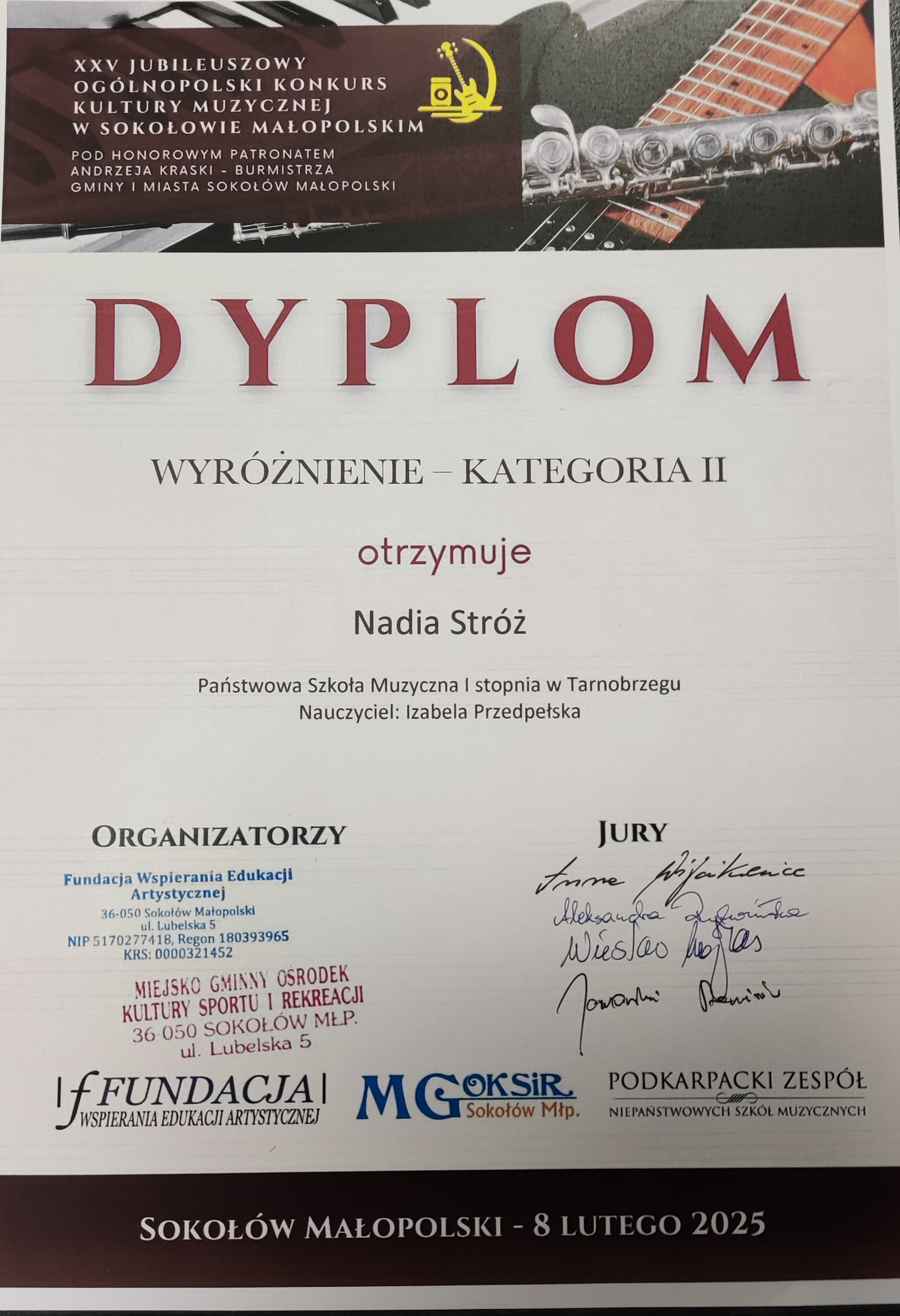 Dyplom wyróżnienia. Na górze znajduje się nazwisko patrona w brązowej ramce, a w tle zdjęcie przedstawiające fragmenty fortepianu, gitary oraz fleta poprzecznego. Po środku nazwisko otrzymującego wyróżnienie oraz nauczyciela. Na dole po lewej stronie organizatorzy, a po prawej podpisy jury. Tekst w kolorze czerwonym i czarnym.