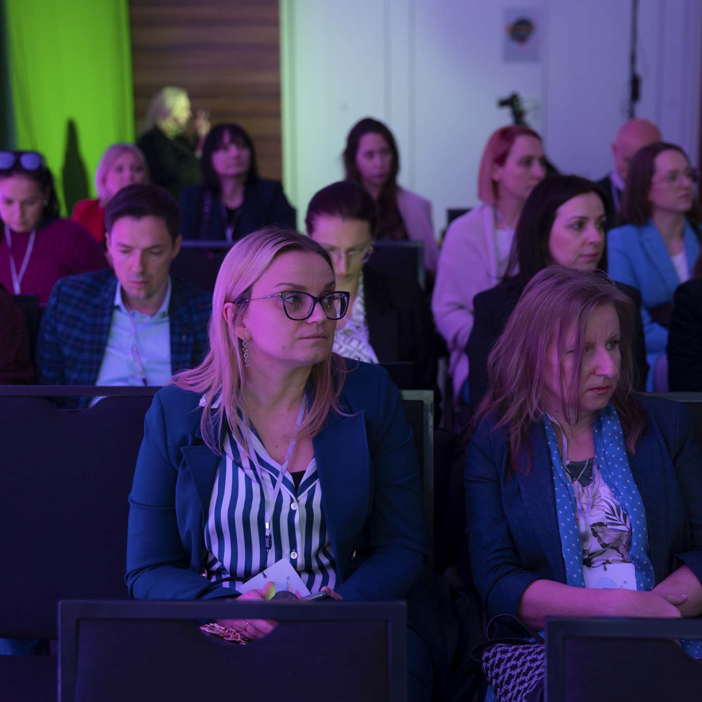 Na krzesłach siedzą uczestnicy i uczestniczki konferencji. Wzrok kierują w stronę sceny.