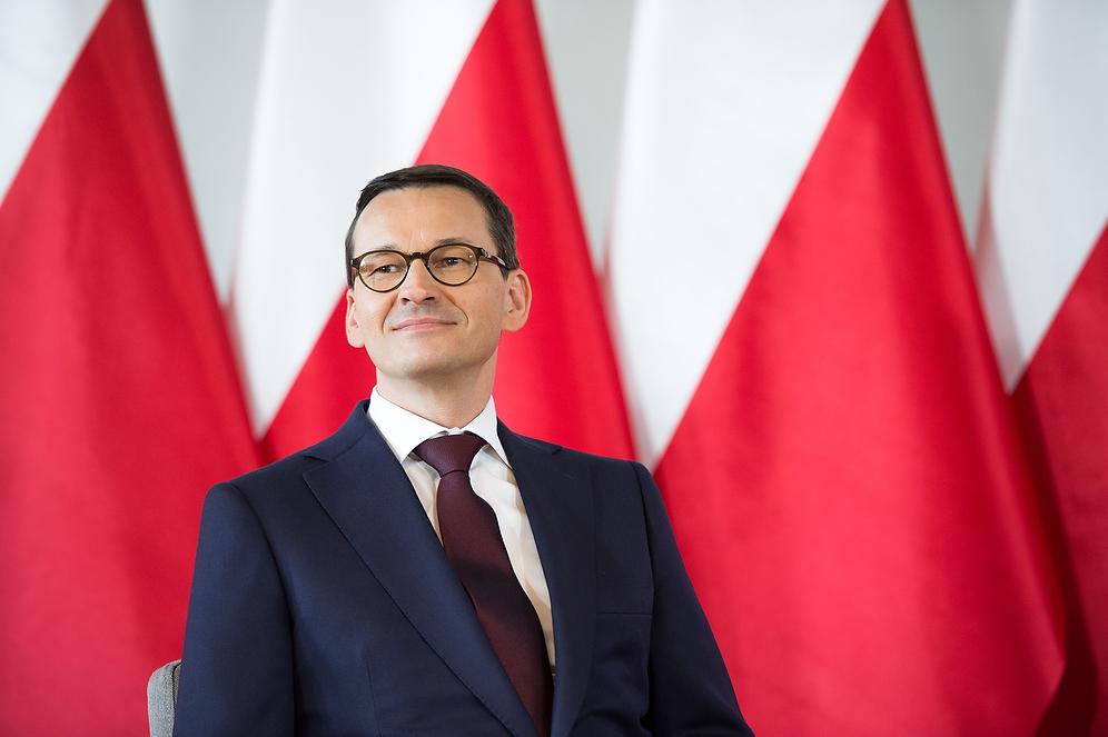 Premier Mateusz Morawiecki na tle flag Polski.