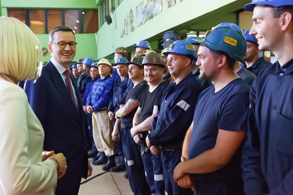 Premier Mateusz Morawiecki śmieje się, rozmawiając z górnikami.