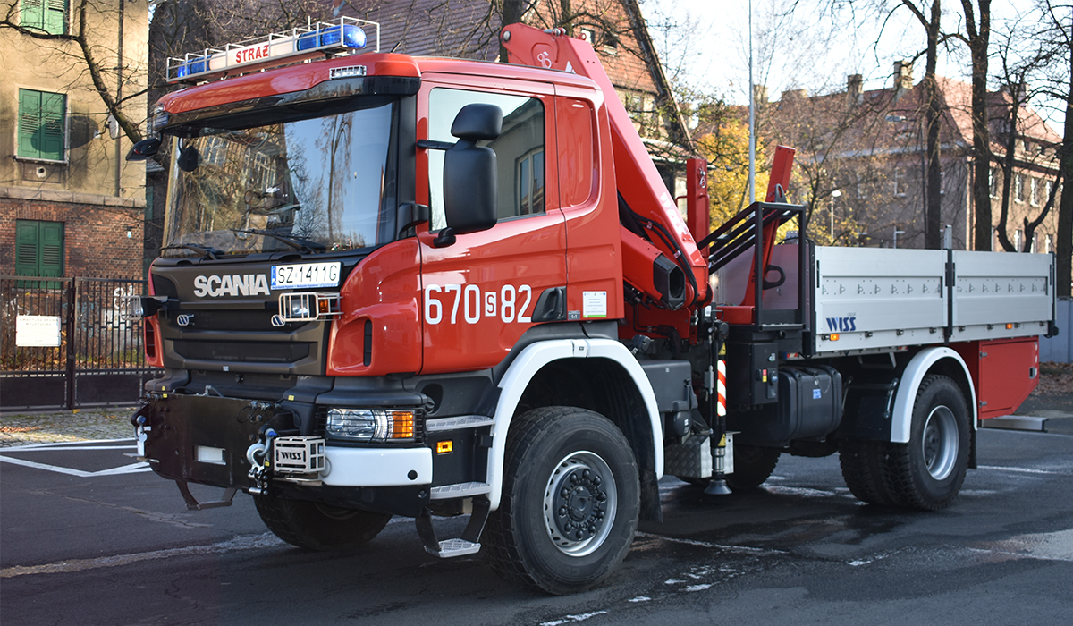 Zdjęcie przedstawia samochód kwatermistrzowski - ciężki Scania P320 na tle budynków znajdujących przy ul. Pawła Stalmacha naprzeciwko Komendy Miejskiej Państwowej Straży Pożarnej w Zabrzu
