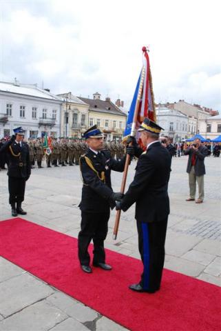 Na sądeckim Rynku Komendant Miejski PSP st.bryg. Janusz Basiaga odbiera sztandar od Komendanta Głównego PSP. W tle widać poddziały uczestniczące w uroczystości.