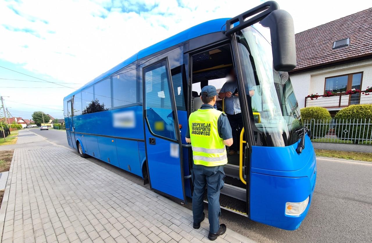 Inspektor stoi obok wejścia do autobusu i pobiera dokumenty od kierowcy.