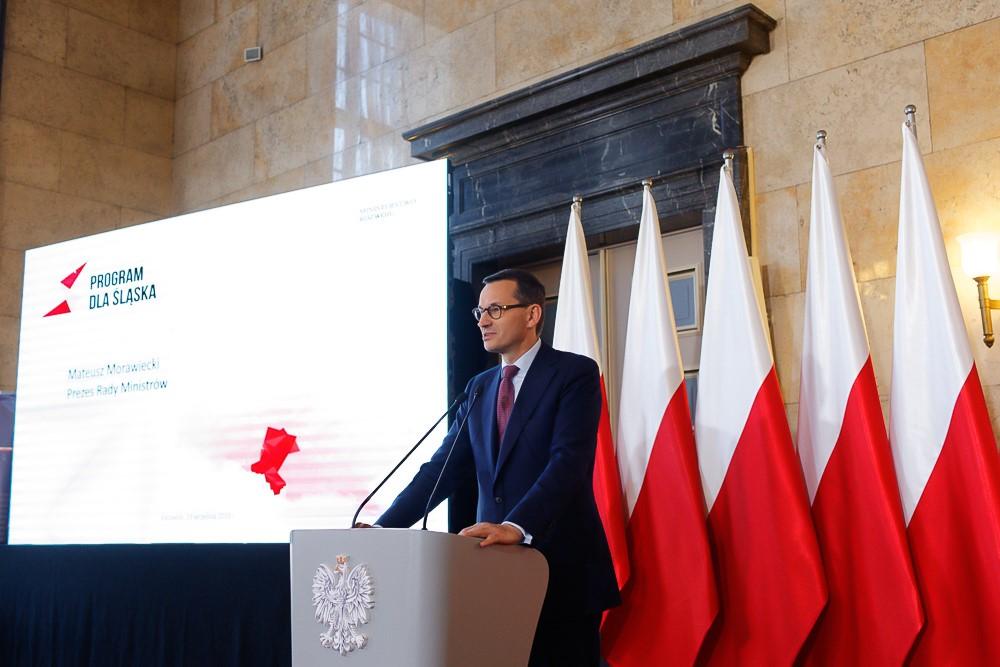 Premier Mateusz Morawiecki przemawia na mównicy na tle flag Polski i napisu "Program dla Śląska".