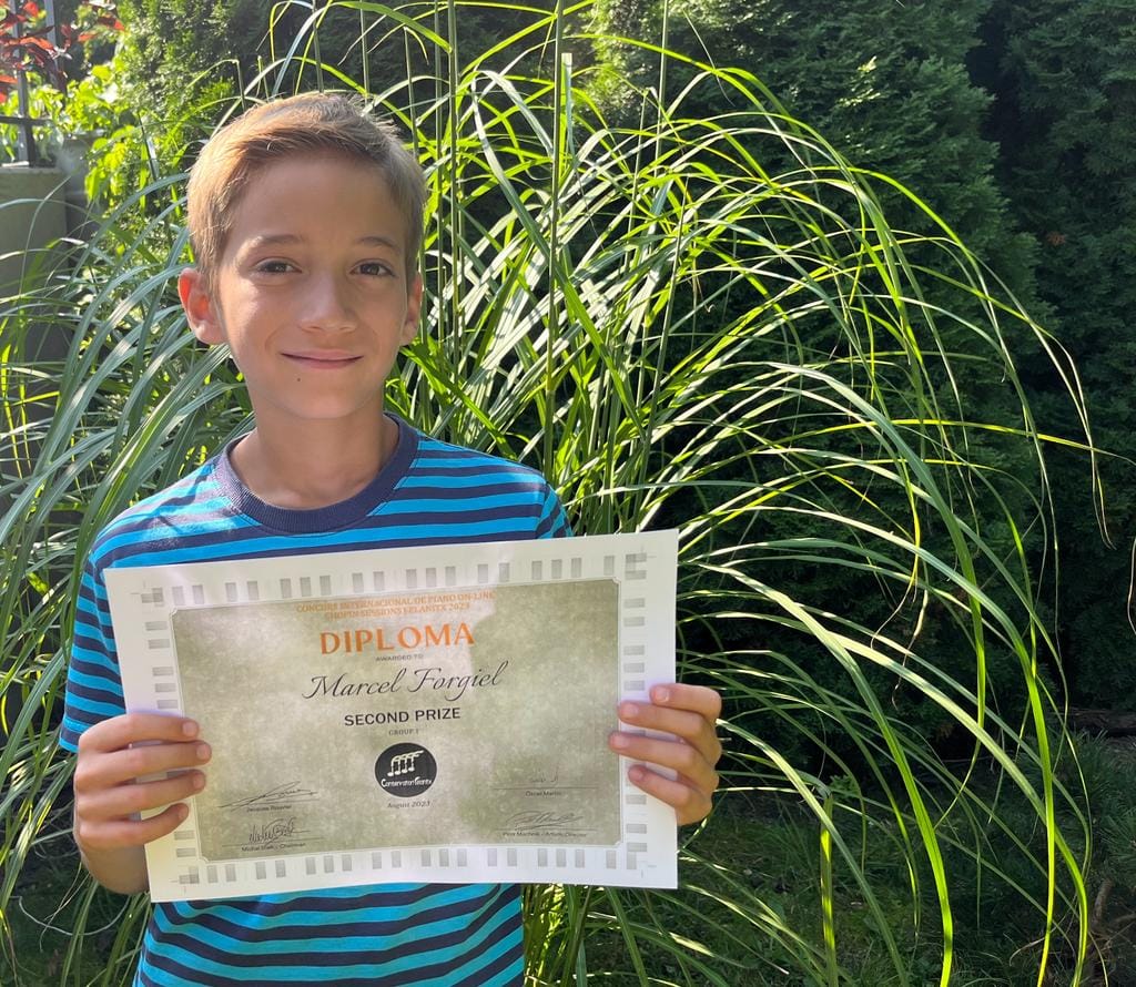 Na zdjęciu widoczny jest uśmiechnięty chłopiec, trzymający w dłoniach dyplom konkursowy.