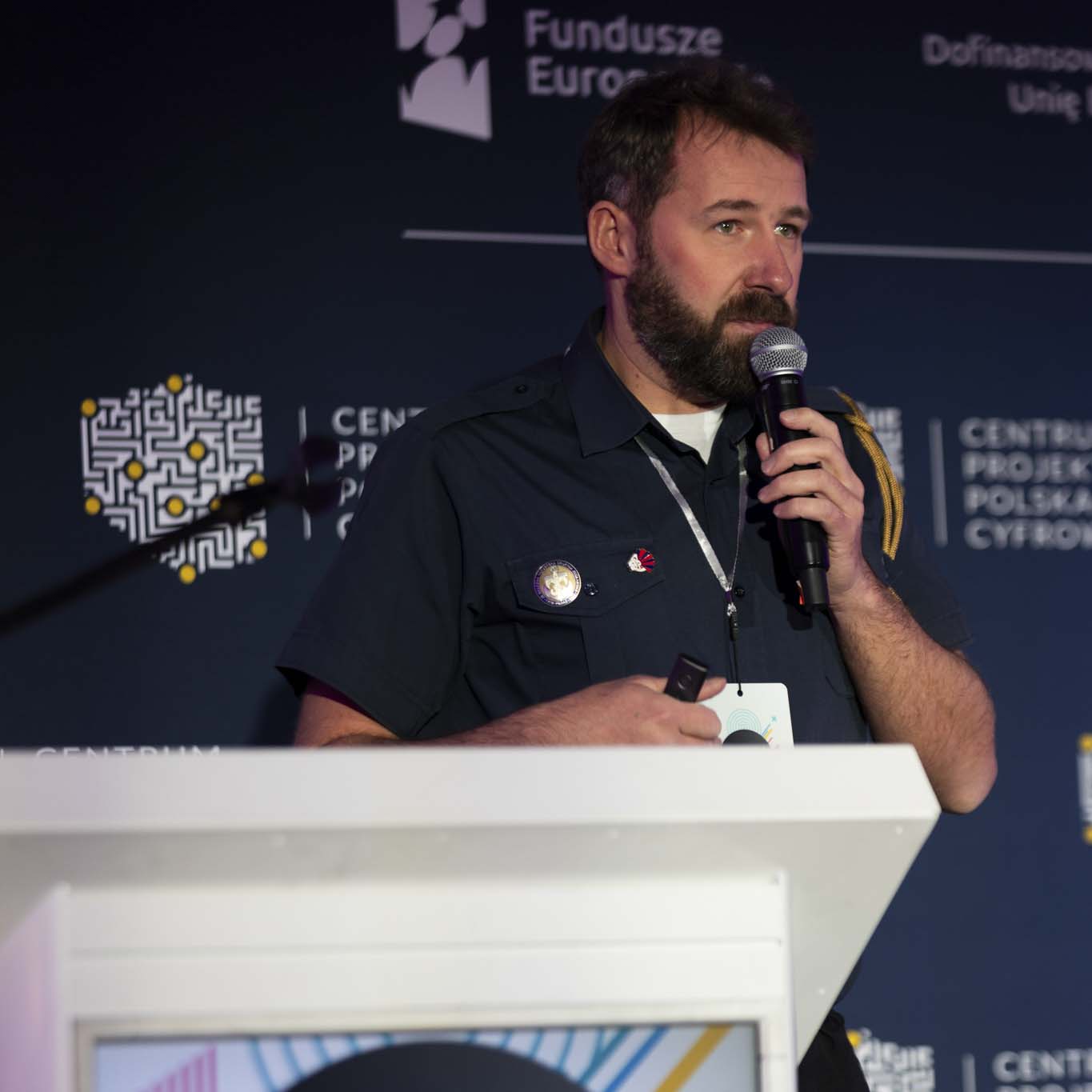 Pan Tomasz Rejmer, instruktor harcerski w stopniu harcmistrza trzyma mikrofon w ręku. Przemawia.
