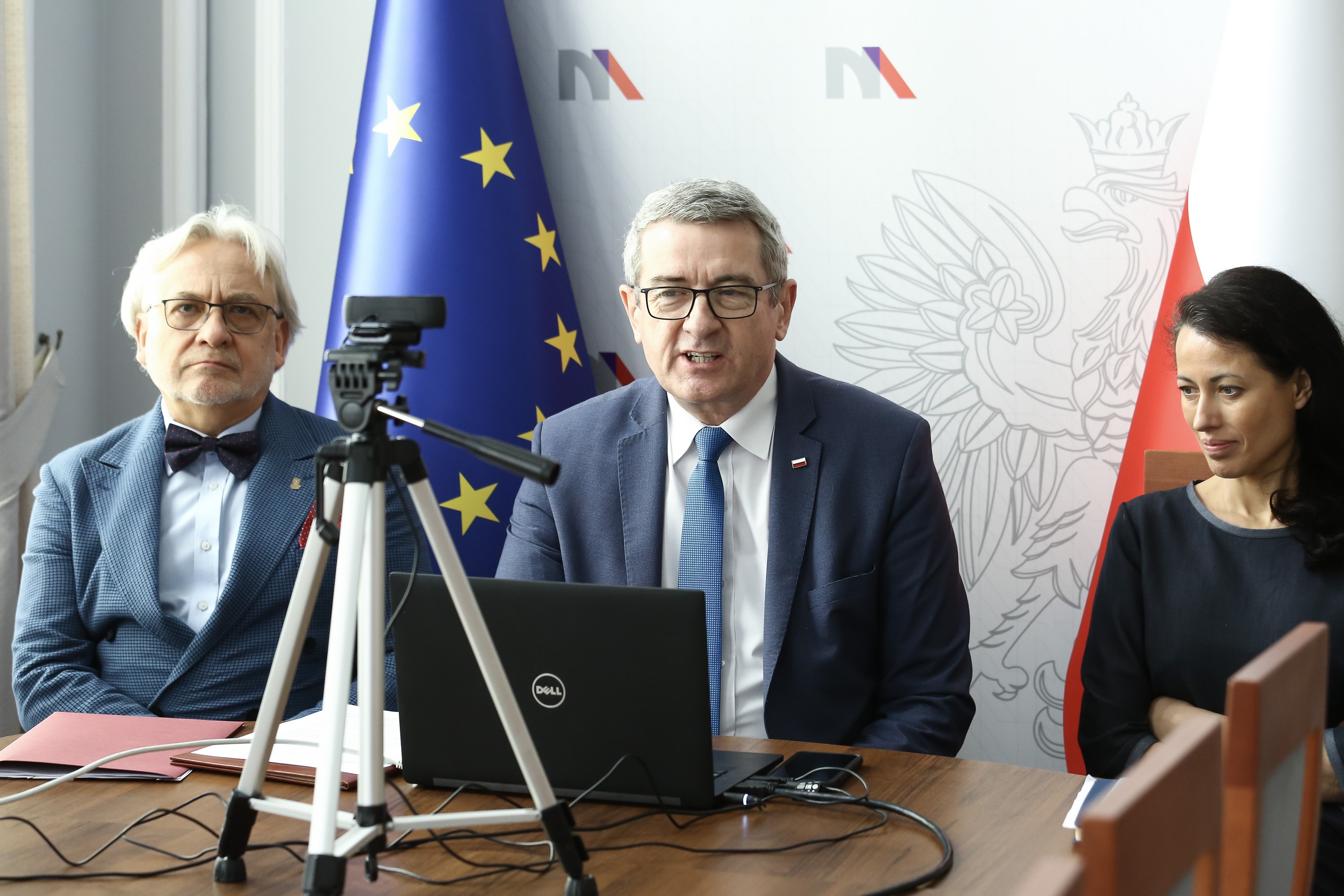 Prof. Maksymowicz, minister Murdzek i dr Budzanowska siedzą za stołem przed kamerą.