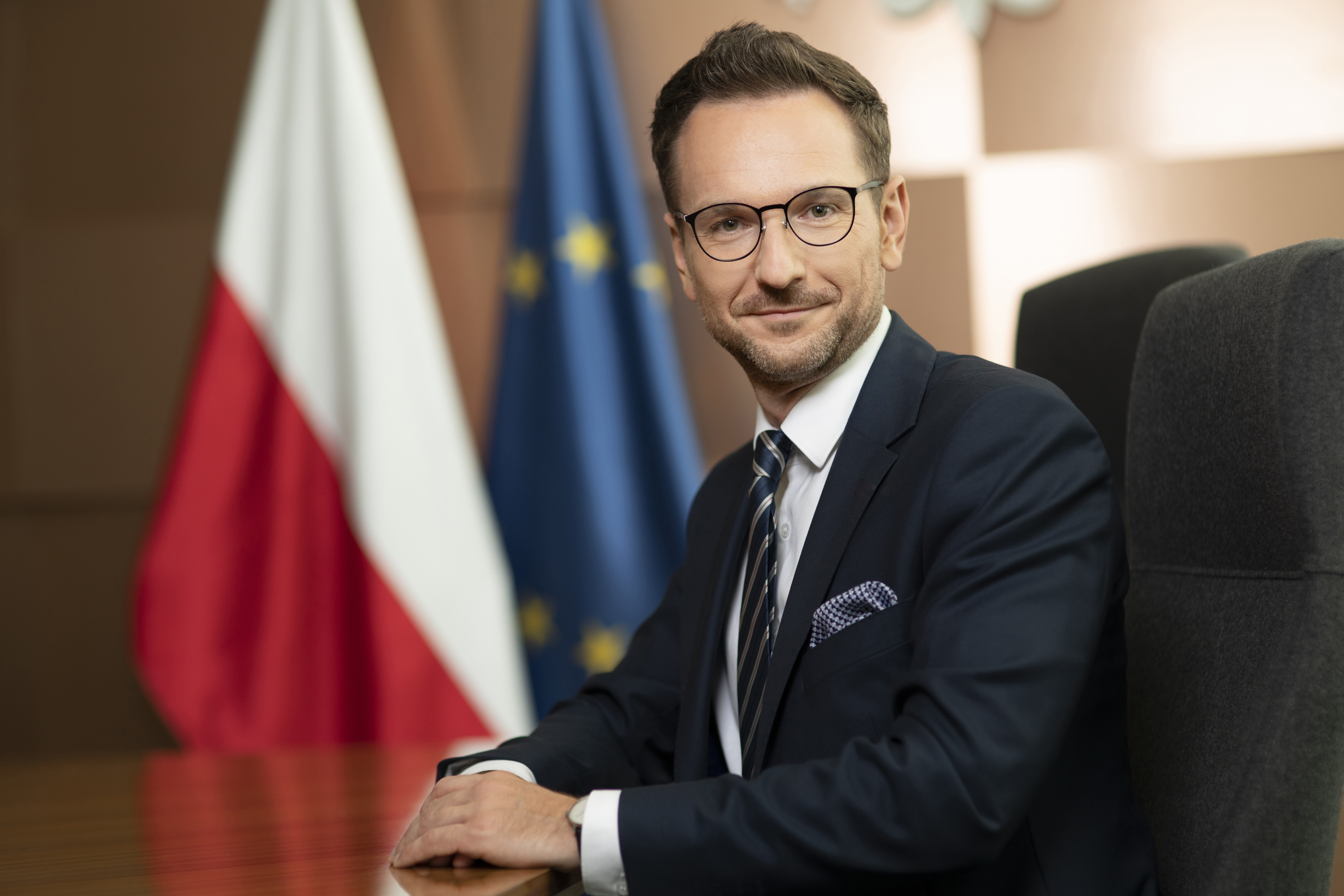 Minister rozwoju i technologii Waldemar Buda, zdjęcie poziome, w tle flagi PL i UE