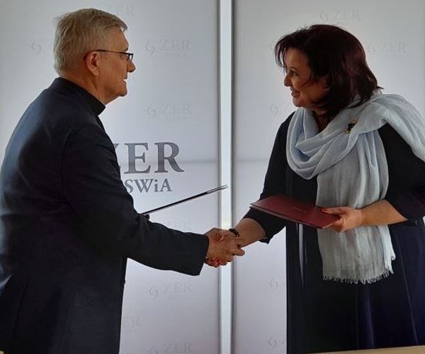 Na zdjęciu jest Pani Małgorzata Zdrodowska, Dyrektor Zakładu Emerytalno-Rentowego Ministerstwa Spraw Wewnętrznych i Administracji oraz ks. prof. dr hab. Ryszard Czekalski, Rektor Uniwersytetu Kardynała Stefana Wyszyńskiego w Warszawie, którzy podają sobie prawe dłonie, a w lewych trzymają czerwone teczki.