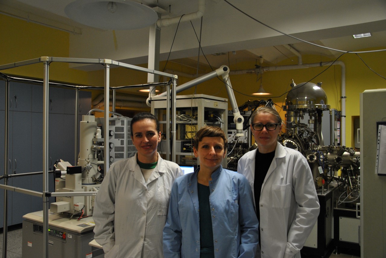 Prof. Iwona Pełech, dr Ewa Ekiert i prof. Ewelina Kusiak-Nejman na tle skaningowego mikroskopu elektronowegoi i spektrometru do badania powierzchni materiałów (XPS).