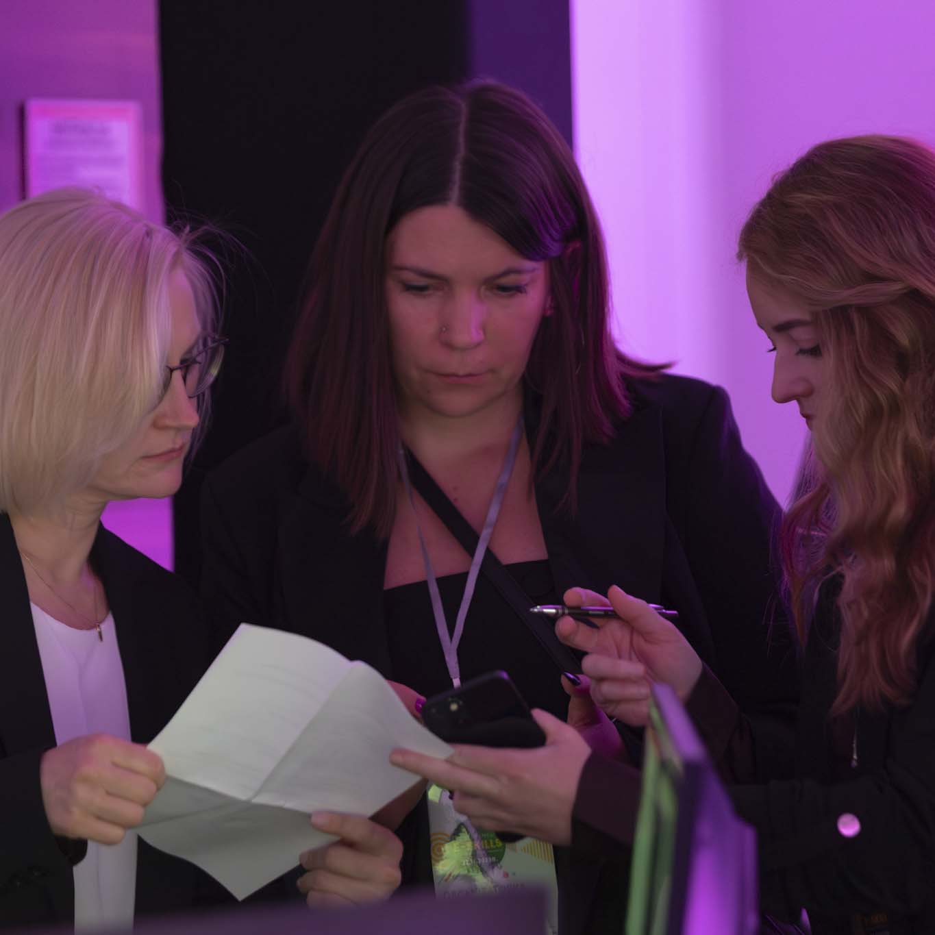 Trzy organizatorki konferencji z zainteresowaniem patrzą na scenariusz konferencji.