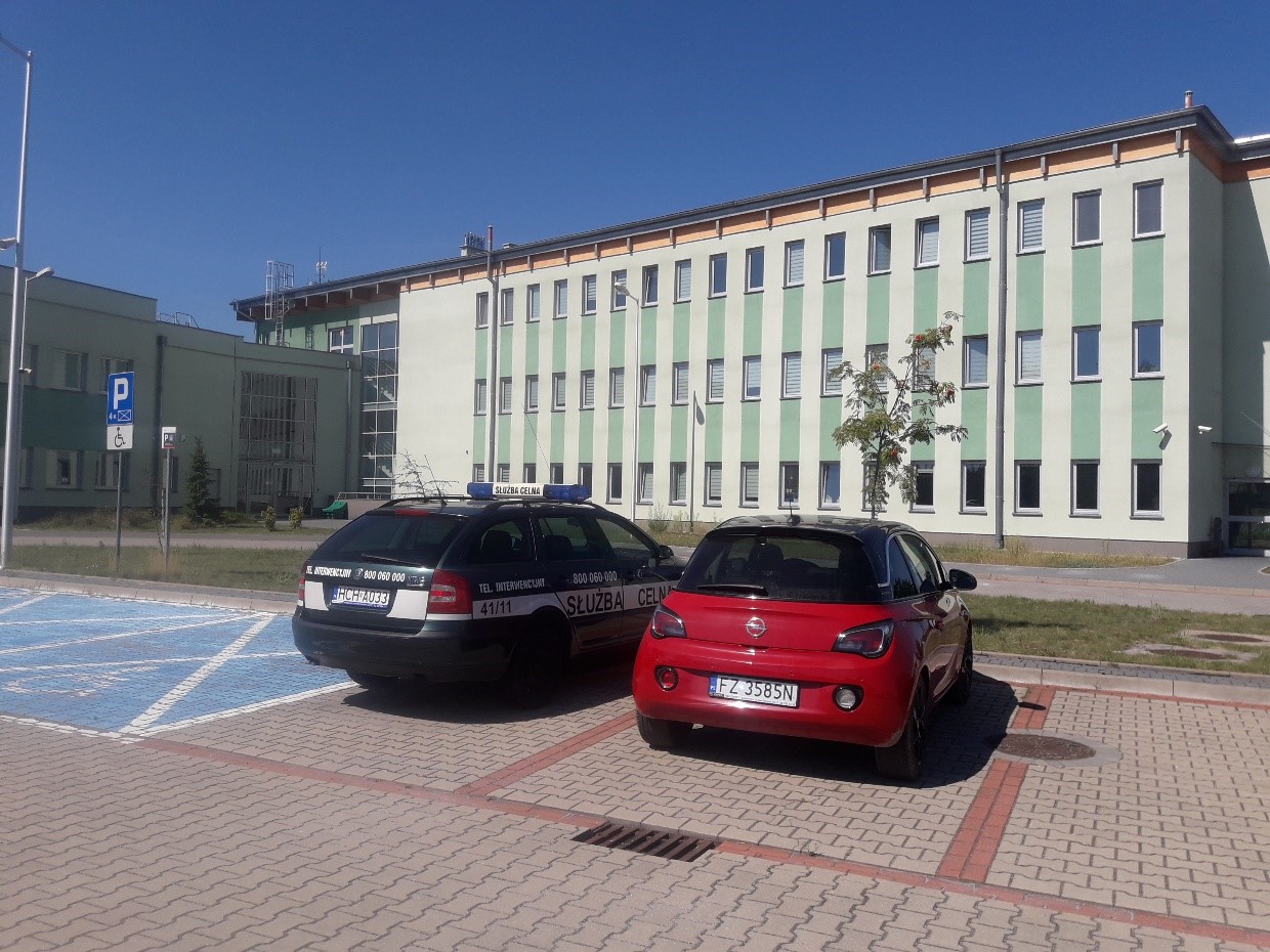 dwupiętrowy budynek w odciniach zieleni, przed pudynkiem parking, w tym parking dla inwalidów
