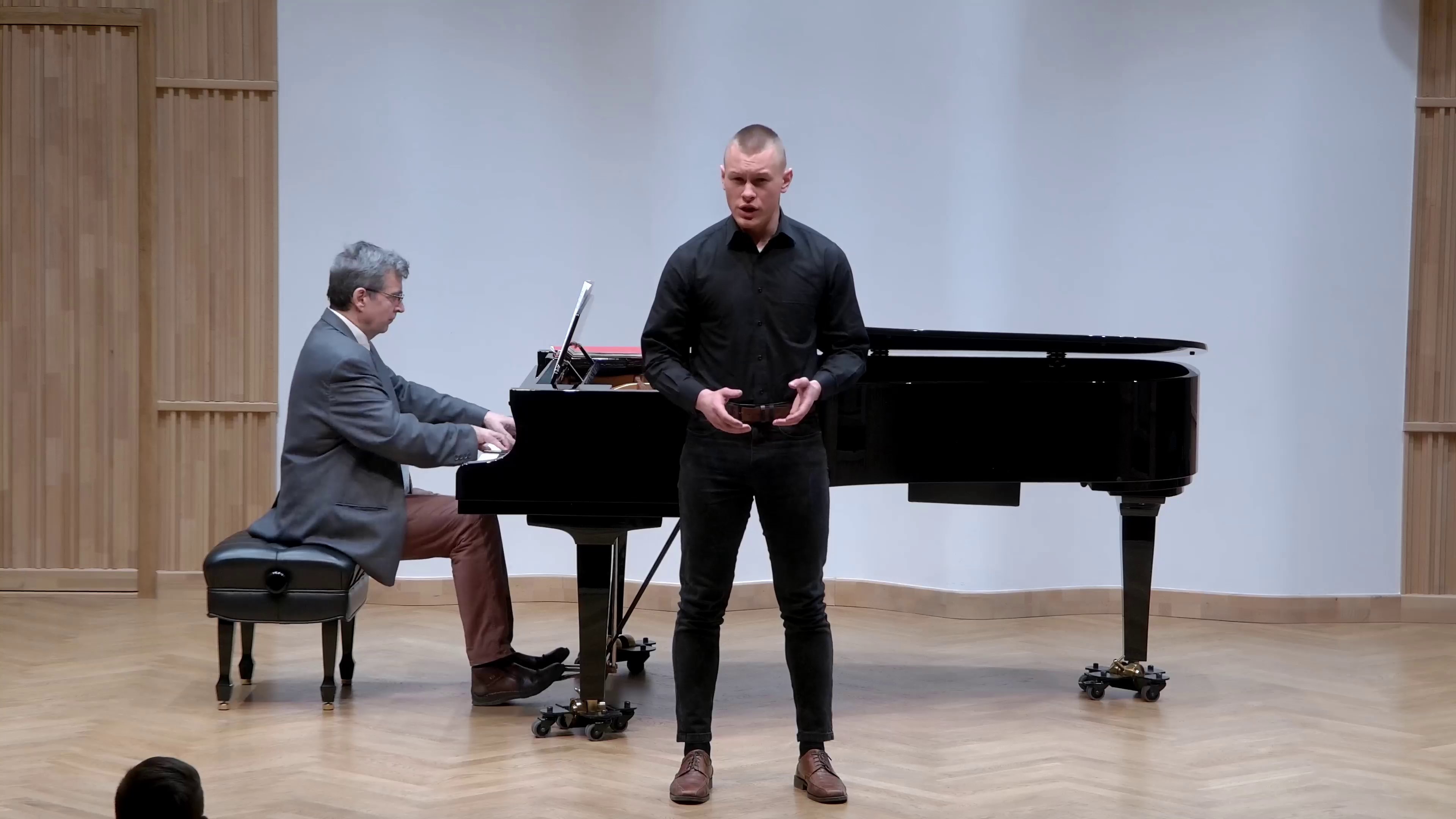 Zdjęcie. Na estradzie występuje wokalista z towarzyszeniem pianisty grającego na dużym czarnym fortepianie.