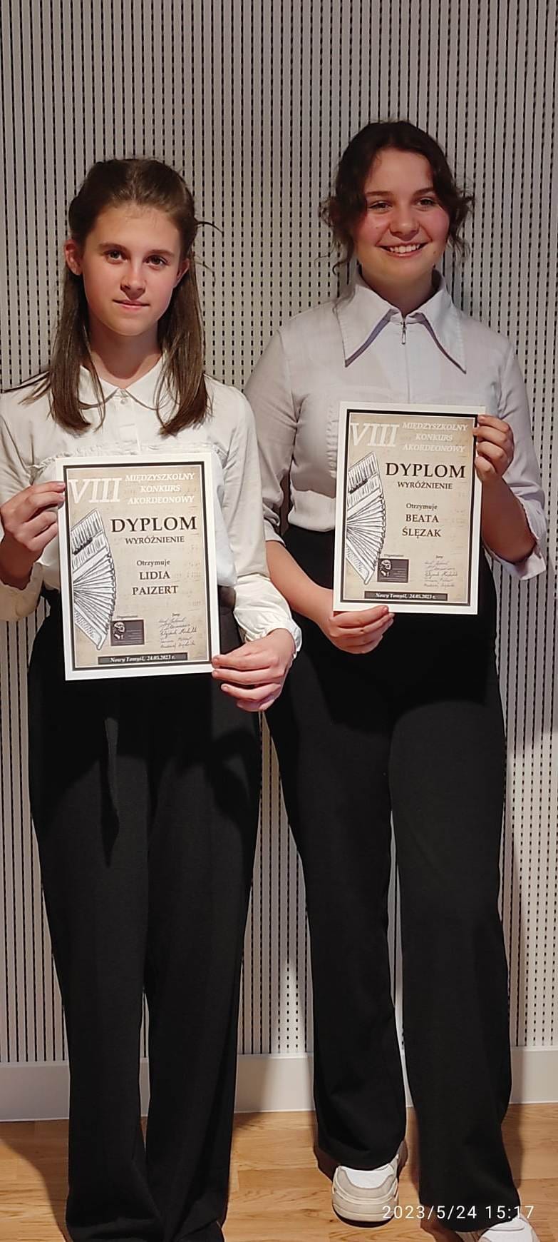Na zdjęciu widać dwie uśmiechnięte uczennice, które trzymają dyplomy.