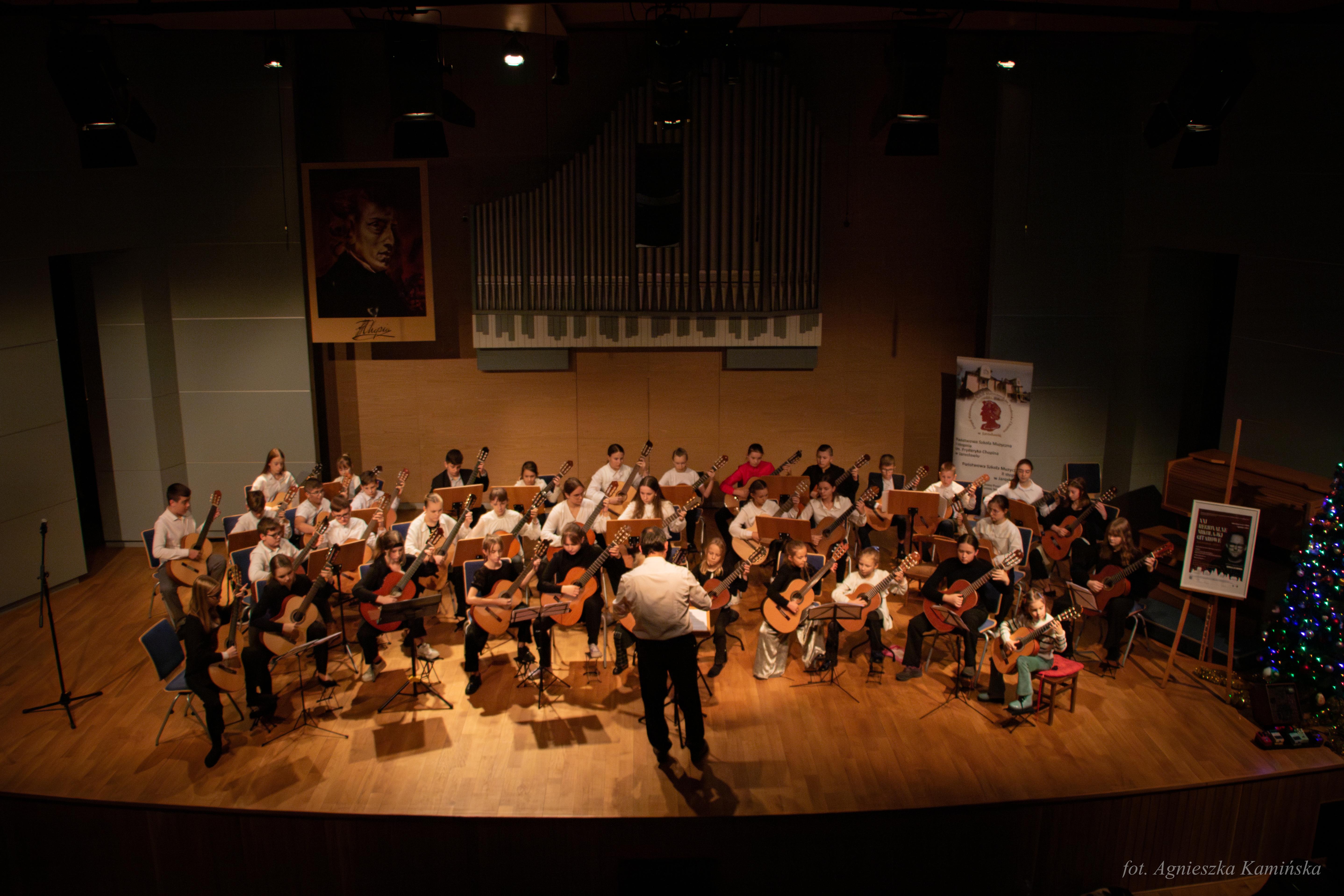 Relacja z XXI Regionalnych Mikołajek Gitarowych - zdjęcie uczniów grających na scenie w ramach orkiestry gitarowej