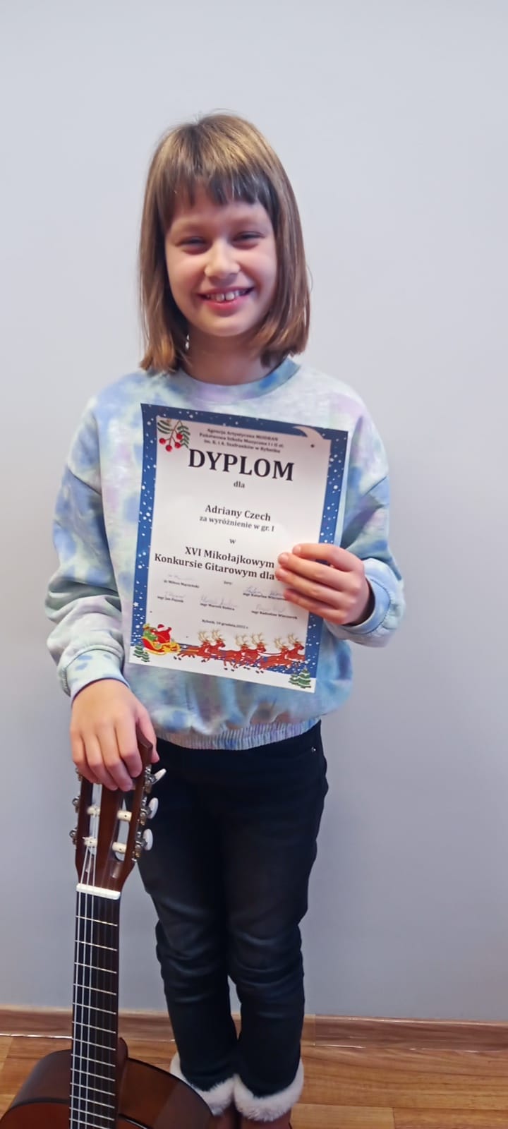 Na zdjęciu znajduje się uczennica Adriana Czech trzymająca w jednej ręce gitarę a w drugiej dyplom konkursu.