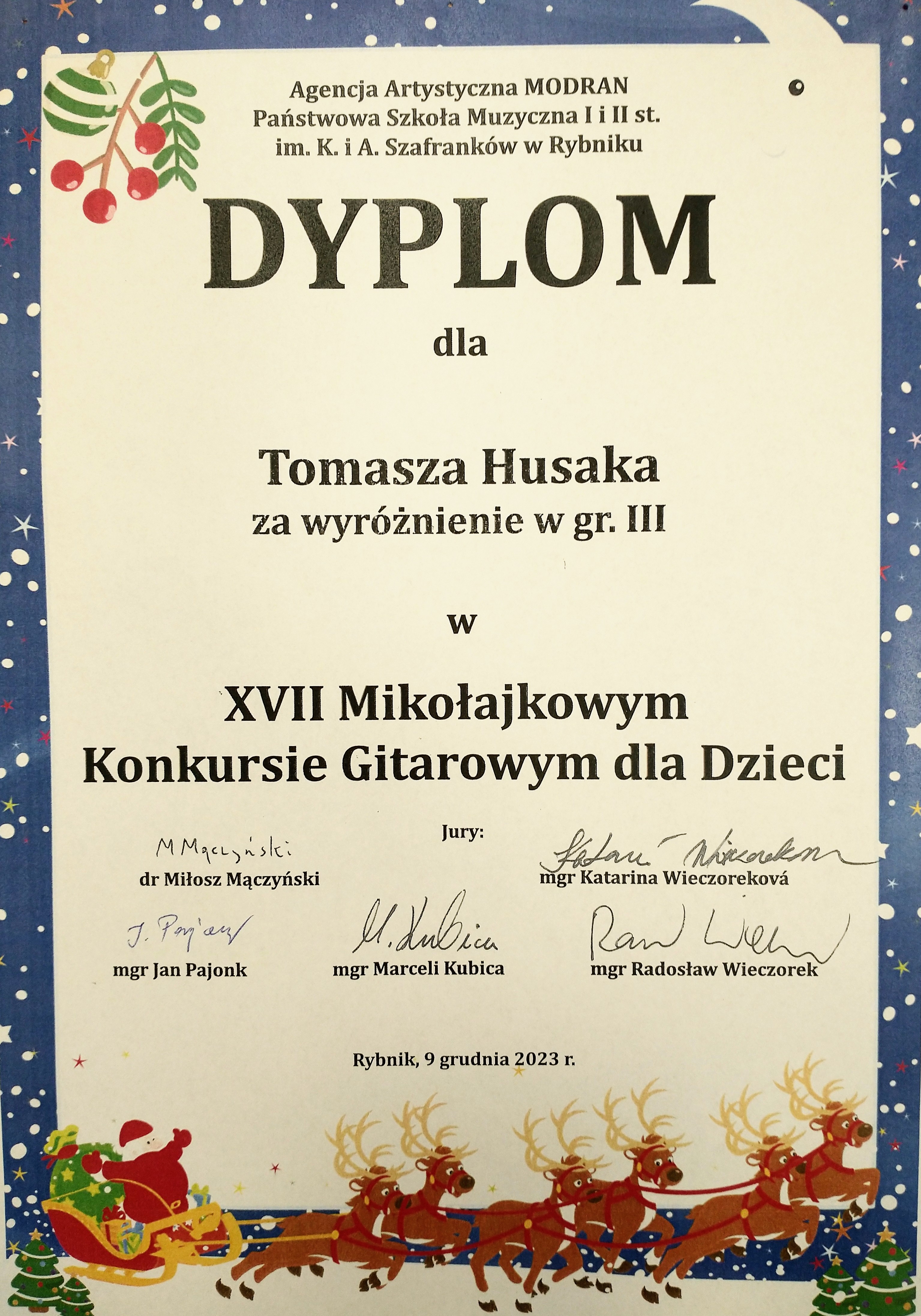 Dyplom kolor kremowy granatowa obwódka z gwiazdkami i śnieżynkami w lewym górnym rogu symbol jarzębiny czerwonej z zieloną gałązką oraz bombką choinkową na samym dole zaprzęg 6 brązowych reniferów ciągnących czerwone sanie z czerwonym Mikołajem siedzącym z rozłożonymi rękoma z tyłu zielony worek prawdopodobnie z prezentami od góry napis agencja artystyczna modran państwowa szkoła muzyczna pierwszego i drugiego stopnia imienia szafranków w Rybniku dyplom dla Tomasza Husaka za wyróżnienie w grupie 3 w XVII mikołajkowym konkursie gitarowym dla dzieci poniżej podpisy jurorów dr Miłosz Mączyński magister Katarina Wieczorkowa magister Jan Pajonk magister Marceli Kubica magister Radosław Wieczorek, Rybnik 9 grudnia 2023