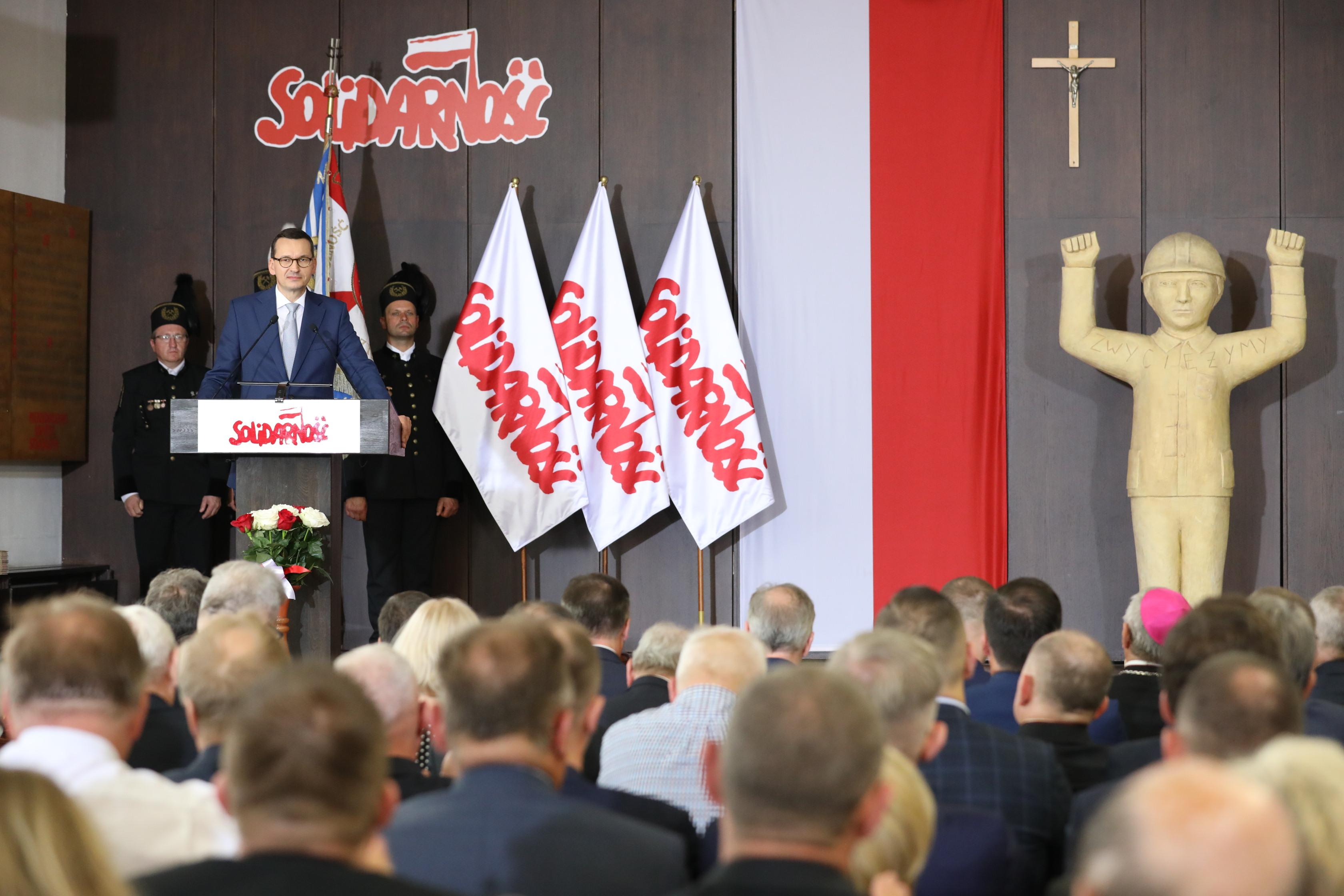 Premier Mateusz Morawiecki stoi podczas przemówienia. 