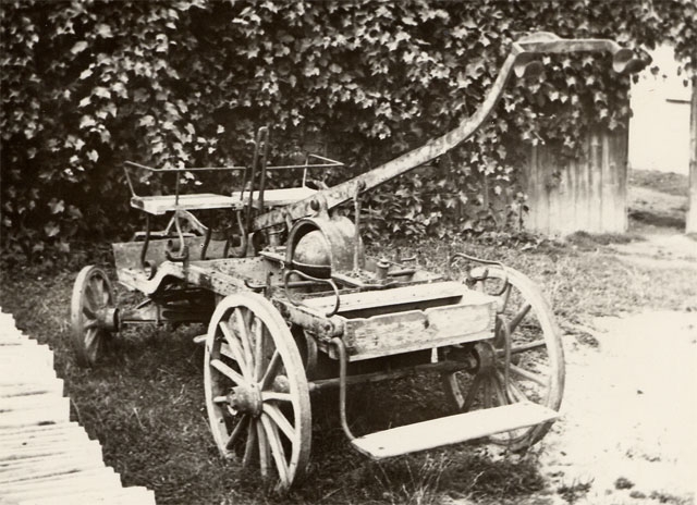 Sikawka ręczna stojąca na trawie, koła drewniane.