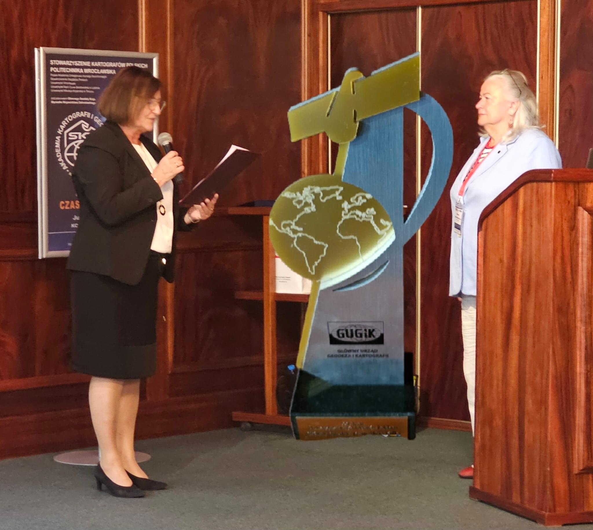 Zdjęcie przedstawia Głównego Geodetę Kraju Alicję Kulkę i Przewodniczącą Zarządu Głównego SKP dr hab. inż. Joannę Bac-Bronowicz podczas IV Akademii Kartografii i Geoinformatyki „Modelowanie czasoprzestrzenne”