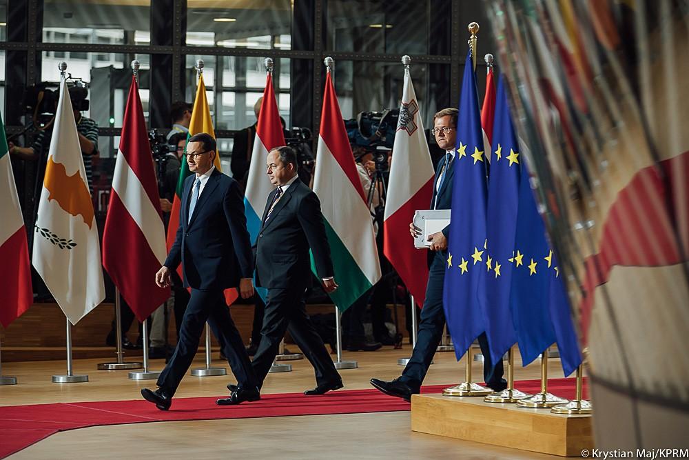 Premier Mateusz Morawiecki wchodzi na czerwony dywam ze wspołpracownikami.